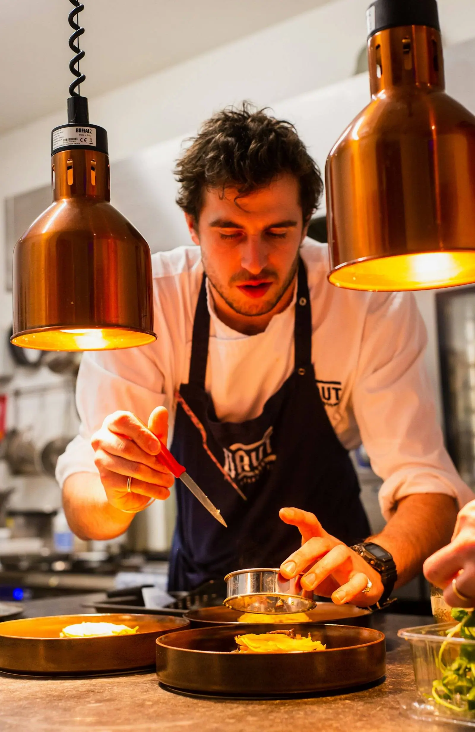 The chef plating under copper lamps
